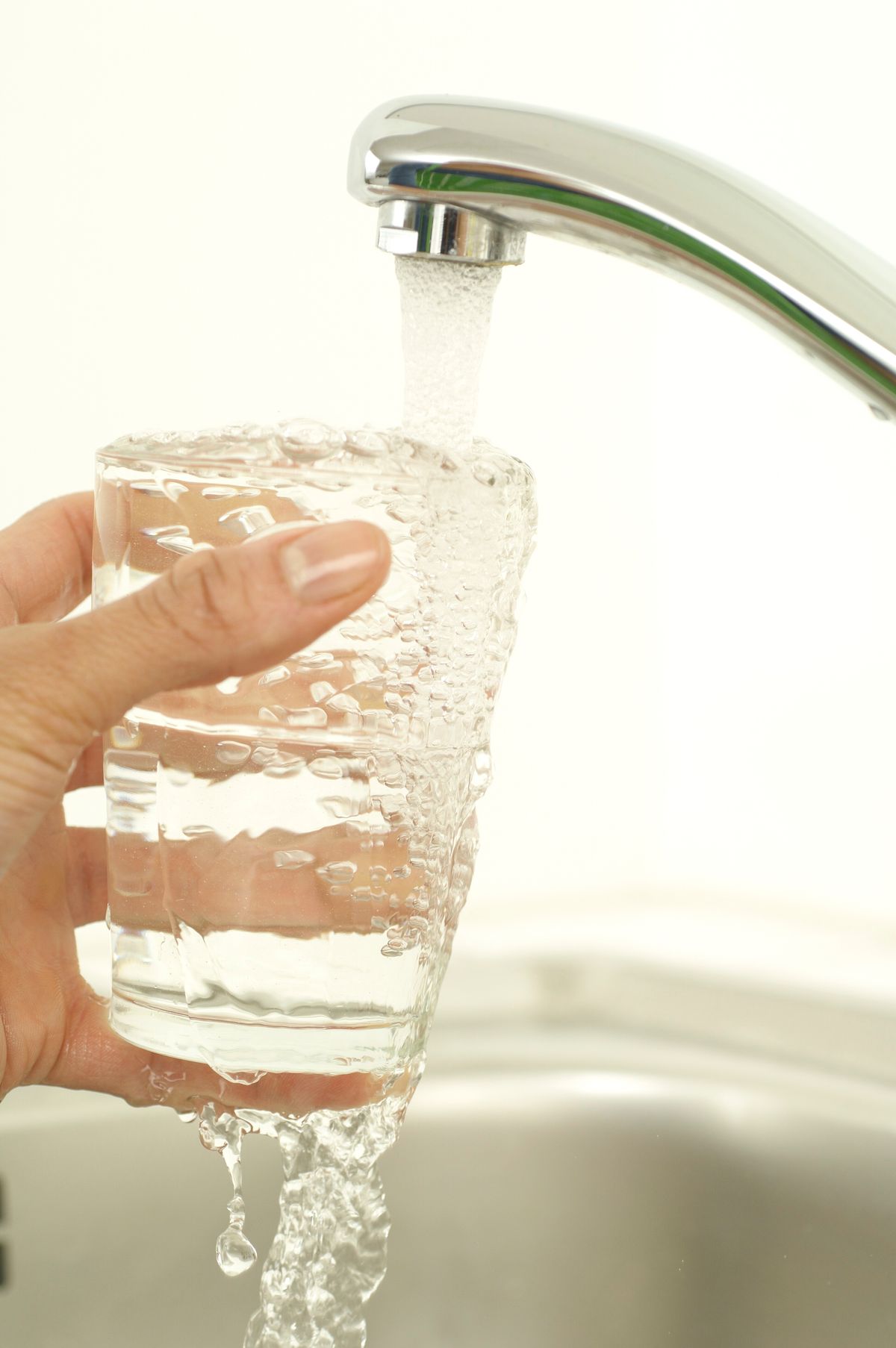 A glass being filled from a tap — municipal supply is the standard source of fluoride, chloramine, and calcium accumulation that produces sharp-bordered brown tips