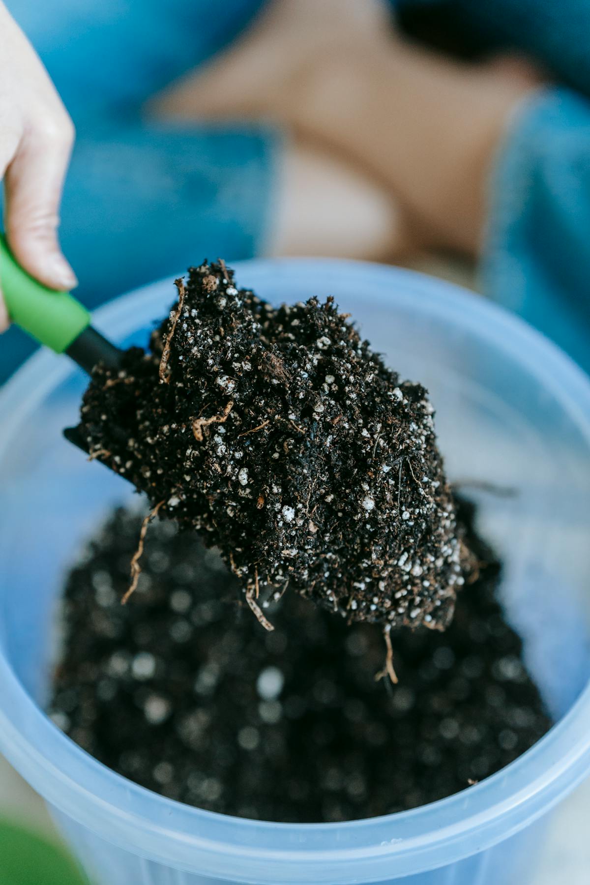 Gardener holding soil on a shovel above a container with a houseplant